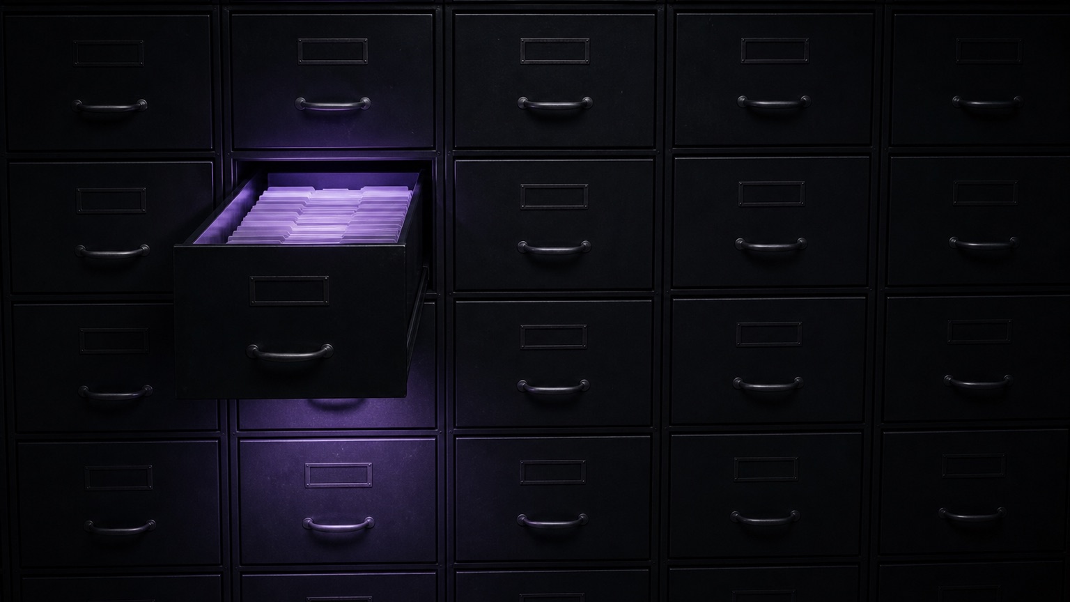 A wall of identical dark filing drawers photographed straight on. One drawer left of centre is pulled fully open, the tabbed index cards inside it lit violet, the glow spilling down the drawer fronts below.
